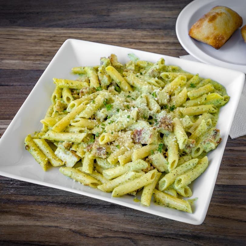 Bianco's Italian Cuisine penne pasta with pesto sauce, parmesan cheese, and chicken, served with bread.