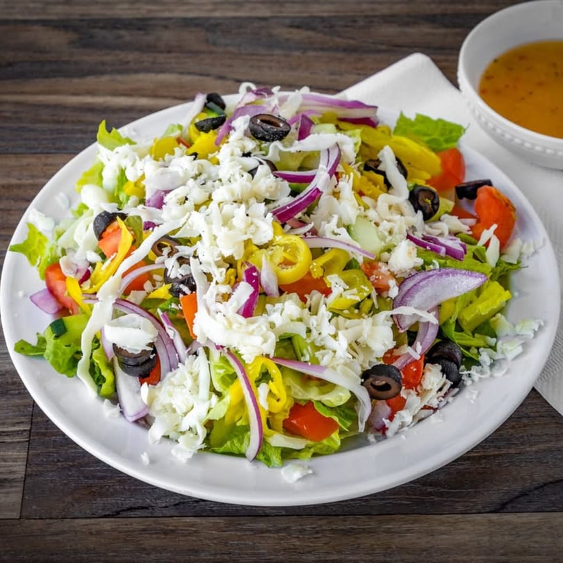 A vibrant Italian salad with lettuce, tomatoes, olives, red onion, and crumbled feta cheese.
