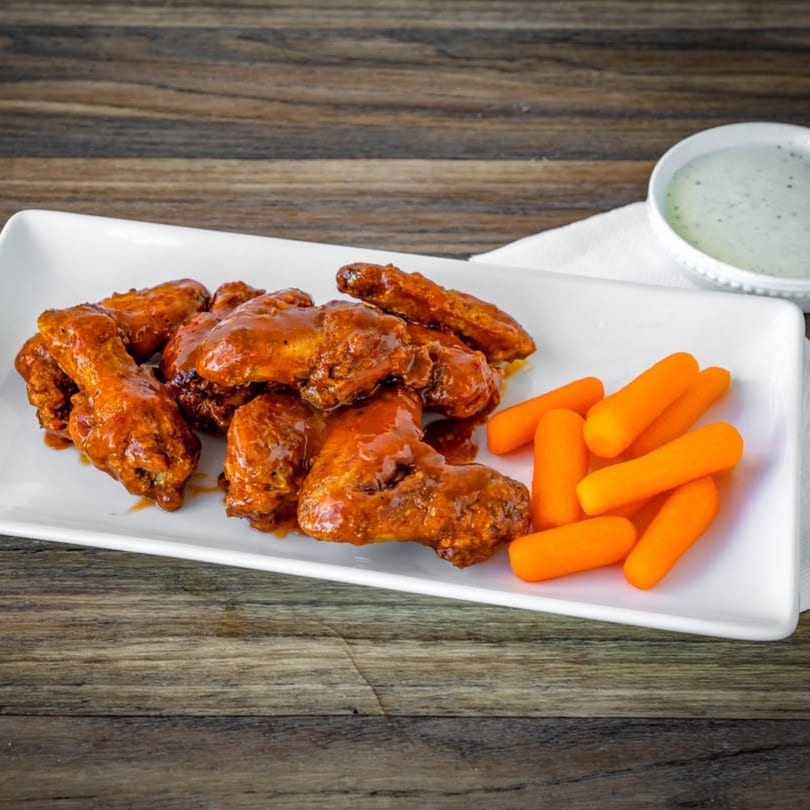 Spicy chicken wings with baby carrots and a side of ranch dressing on a white plate.