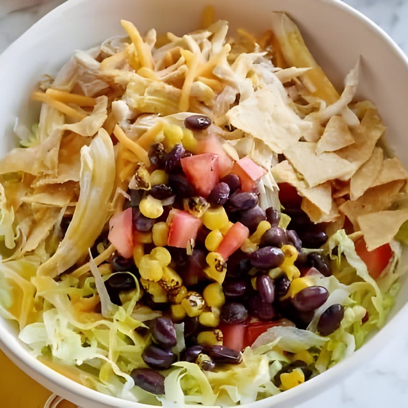 A vibrant salad with lettuce, black beans, corn, diced tomatoes, shredded cheese, and tortilla strips.